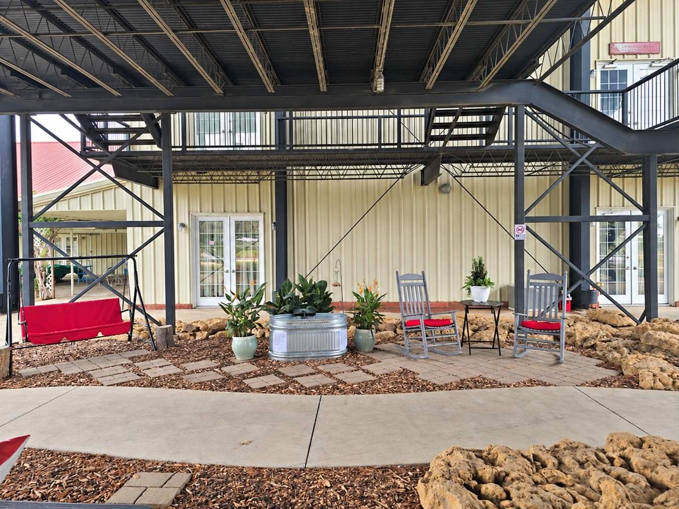 The covered courtyard under the pavilion: rocking chairs, a red porch swing and potted plants on a flagstone patio between the studio doors.