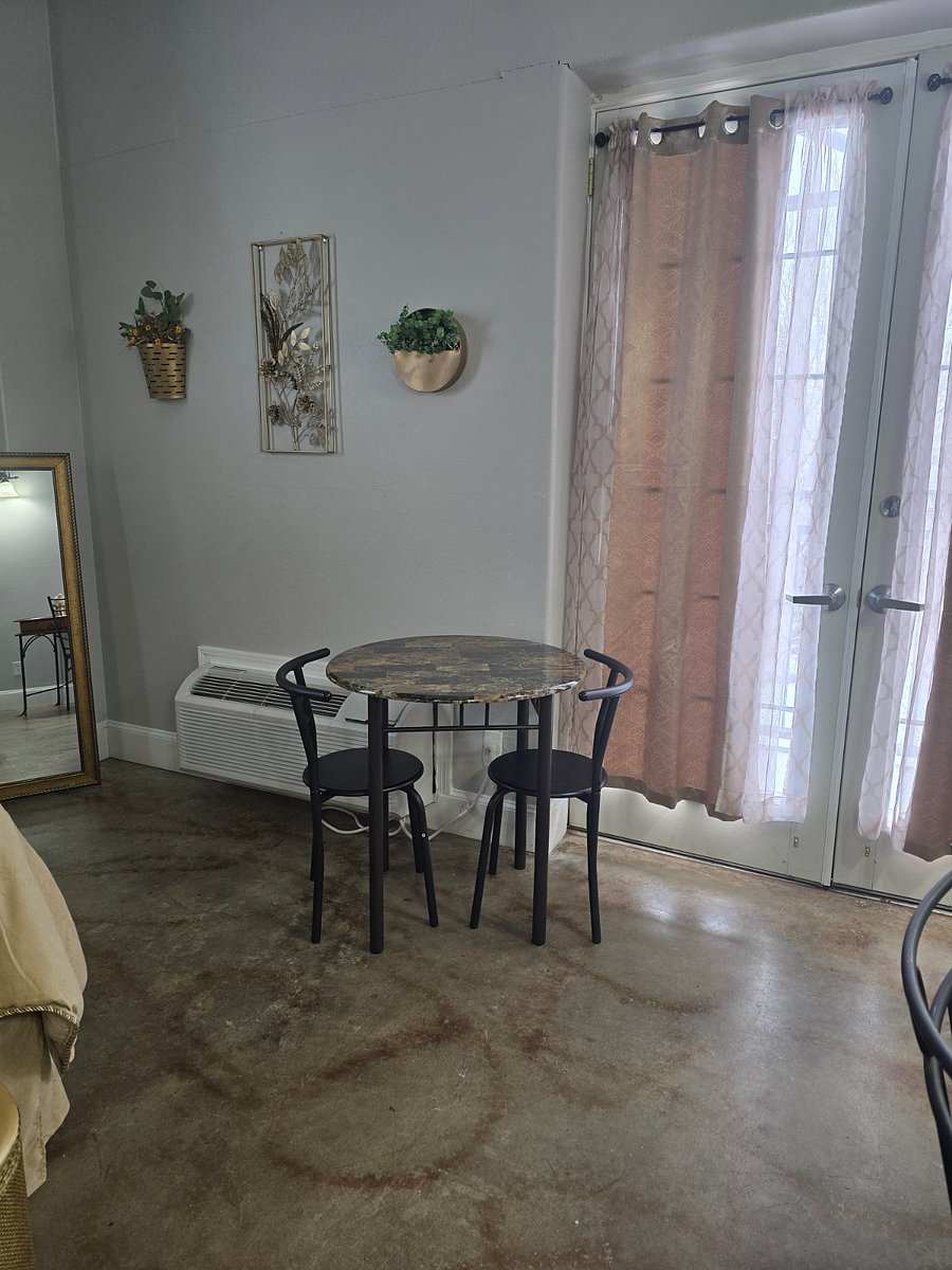 Studio 203: a round bistro table with two chairs by French doors with sheer curtains, a floor mirror and wall plants.